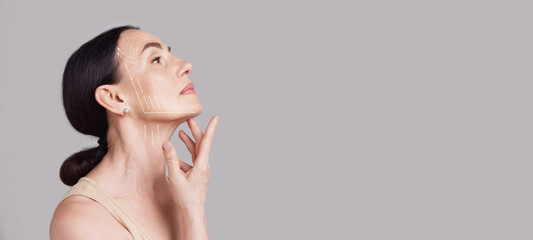 beautiful senior woman with lifting arrows showing facial anti-aging treatment on skin against grey 