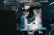 © dikushin - Wide shot of cooperating team of surgeons processing surgical operation in dark operating room modern hospital emergency department. Doctors in sterile gloves, surgical uniforms and masks.