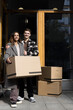© Maskot - Portrait of smiling multiracial couple standing with boxes in front of apartment