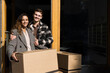 © Maskot - Portrait of smiling man embracing woman holding cardboard box in front of apartment