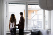 © Maskot - Couple looking through window while standing in new home