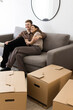 © Maskot - Happy couple embracing while sitting on sofa by cardboard boxes at home