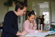 © Maskot - Father sitting next to excited daughter doing homework at home