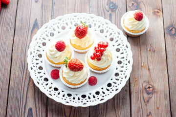 Wall Mural - Vanilla cupcakes decorated with fresh strawberry, raspberry and red currant on rustic wooden background
