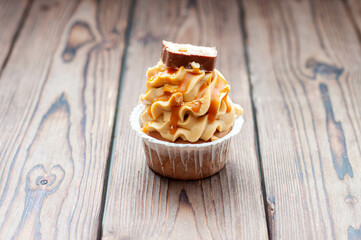 Wall Mural - Delicious chocolate cupcakes with peanut butter frosting, chocolate bites and salted caramel sauce on rustic wooden background
