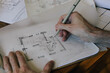 © Maskot - Cropped hands of male architect sketching blueprint on paper at desk in home office