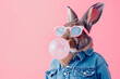 A stylish bunny in a denim jacket and sunglasses blowing a pink bubble gum bubble