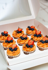 Wall Mural - Orange cupcakes with fresh berries and buttercream frosting in the gift box