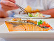 Selective focus of grilled salmon steak on white plate, Japanese food style with blurry women hand and chopsticks