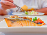 Fototapeta Tulipany - Selective focus of grilled salmon steak on white plate, Japanese food style with blurry women hand and chopsticks