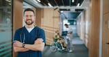 Fototapeta  - Portrait of attractive successful Caucasian doctor in uniform with stethoscope looking at camera and smiling. Happy professional medical worker standing at corridor with patient on background.