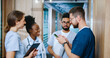 © ihorvsn - Side view portrait of diverse multi-age group of professional medical staff conversing in modern hospital corridor during break. Successful doctors and nurses using devices online.