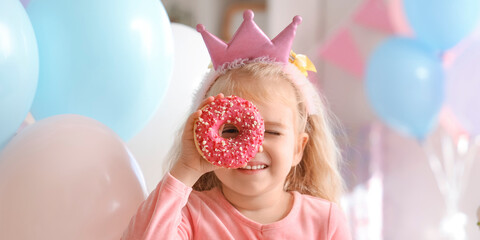 Wall Mural - Cute little girl in crown with doughnut celebrating Birthday at home, closeup