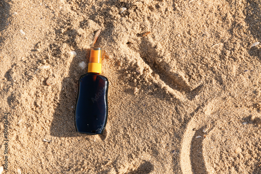 Bottle of sunscreen cream on sand at sea beach