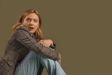 Wall Mural - Scared mature woman sitting on green background