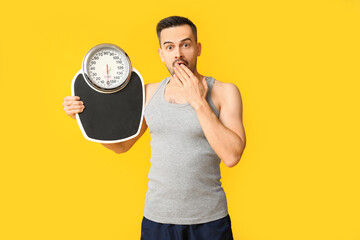 Canvas Print - Handsome sporty shocked man with scales on yellow background. Weight loss concept