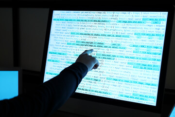 Hacker pointing at computer screen in dark room, closeup