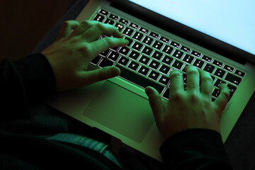 Hacker using laptop in dark room, closeup