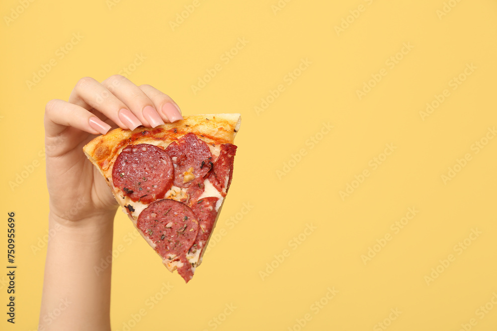 Female hand holding tasty pizza slice on yellow background
