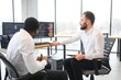 © Serhii - Two diverse colleagues traders talking to each other, sitting in the office in front of multiple computer screens. Stock trading, people, business concept