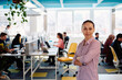© .shock - Portrait of young smiling business woman in creative open space coworking startup office. Successful businesswoman standing in office with copyspace. Coworkers working in background