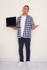 Wall Mural - Full body portrait of a man carrying laptop with confused expression