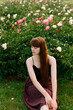 © Amor Burakova/Stocksy - Portrait of young woman sitting on peony garden