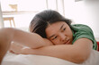 Unhappy asian Thai woman leaning on white cough sofa while resting head on arm with sadness, sitting on wooden floor, thinking something sad, living alone in room apartment. 