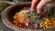 © Justlight - A bowl filled with dried herbs and flowers with a hand reaching in to mix them together. The caption reads homemade herbal blends for teas tinctures and bath salts.