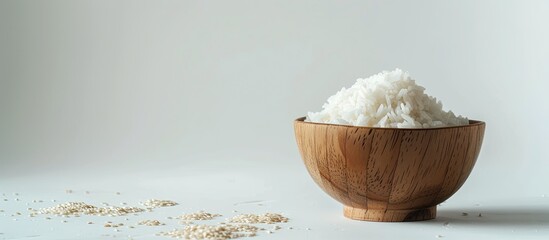A wooden bowl filled with rice is sitting on top of a clean white table. The grains of rice are neatly arranged, creating a rich texture in the bowl.