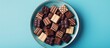 A plate filled with assorted chocolates rests on a vibrant blue background. The variety of chocolate bars is arranged neatly, tempting anyone who sees them to indulge in their rich flavors.