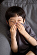 © ChaoShu Li/Stocksy - Little asian boy sitting on sofa at home and smiling