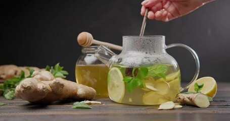 Wall Mural - woman mixing freshly brewed organic herbal tea with ginger, mint and lemon in a glass teapot