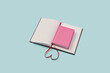 © Yaroslav Danylchenko/Stocksy - Pink book laid on open blank notebook.