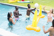 Diverse group of friends enjoy a game of volleyball in a pool, with a yellow inflatable nearby
