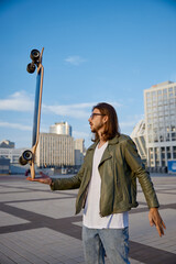 Hipster guy holding skateboard on hand in balance doing trick