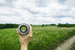 Looking to the green summer field through lens in hand. Point of view. Selective focus.