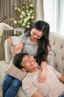 © bongkarn - A happy young Asian couple enjoys talking and relaxing on a sofa in the living room together.