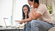© bongkarn - An unhappy young Asian couple is arguing about high domestic bills on a sofa in the living room.