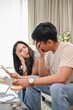 © bongkarn - An unhappy young Asian couple is arguing about high domestic bills on a sofa in the living room.