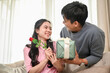 © bongkarn - A caring and romantic Asian man is surprising his girlfriend with a present and flowers at home.