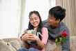 © bongkarn - A caring and romantic Asian man is surprising his girlfriend with a present and flowers at home.