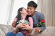 © bongkarn - A romantic Asian wife is kissing her husband's cheek on a couch to thank him for a special present.