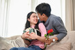 © bongkarn - A caring and romantic Asian man is surprising his girlfriend with a present and flowers at home.