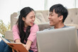 © bongkarn - A cheerful young Asian couple is laughing and enjoying talking while working at home together.