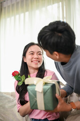 A caring and romantic Asian man is surprising his girlfriend with a present and flowers at home.