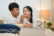 © bongkarn - Happy Asian couple is having a fun time in bed, enjoying popcorn while watching a movie on a laptop.