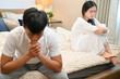 © bongkarn - A sad Asian wife in pajamas is sitting separately with her husband on bed after their argument.