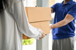 © bongkarn - A woman receiving cardboard parcel boxes from a delivery man in front of the house's door.