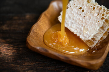 Wall Mural - Pour honey into wooden cup and honeycomb on natural background.